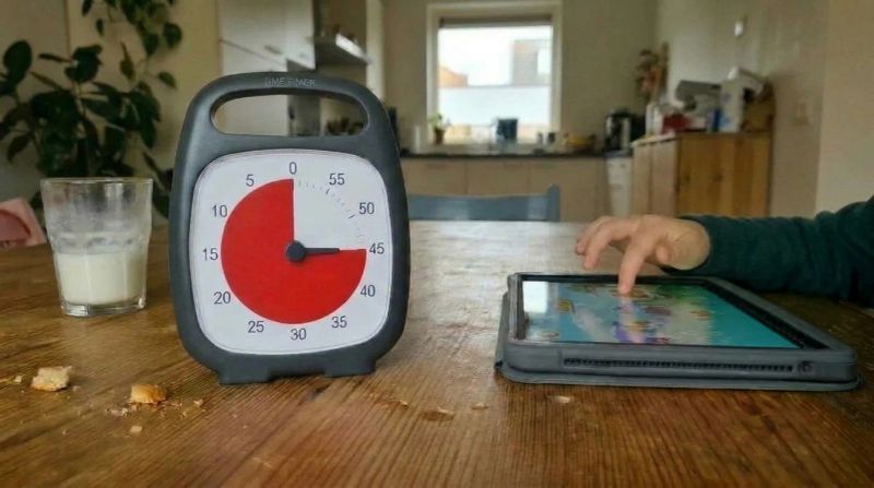 Visuele timer met rode schijf naast een kind dat op een tablet een spelletje speelt