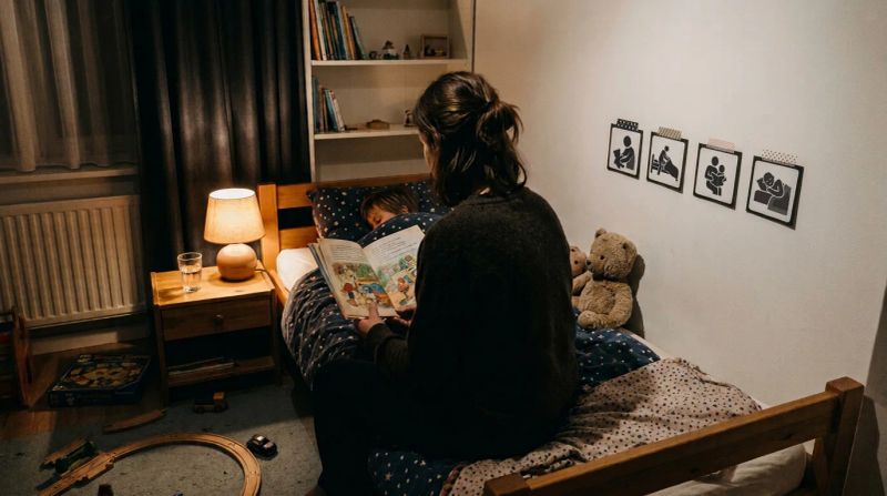 Ouder leest voor aan de rand van een kinderbed, met picto's aan de muur